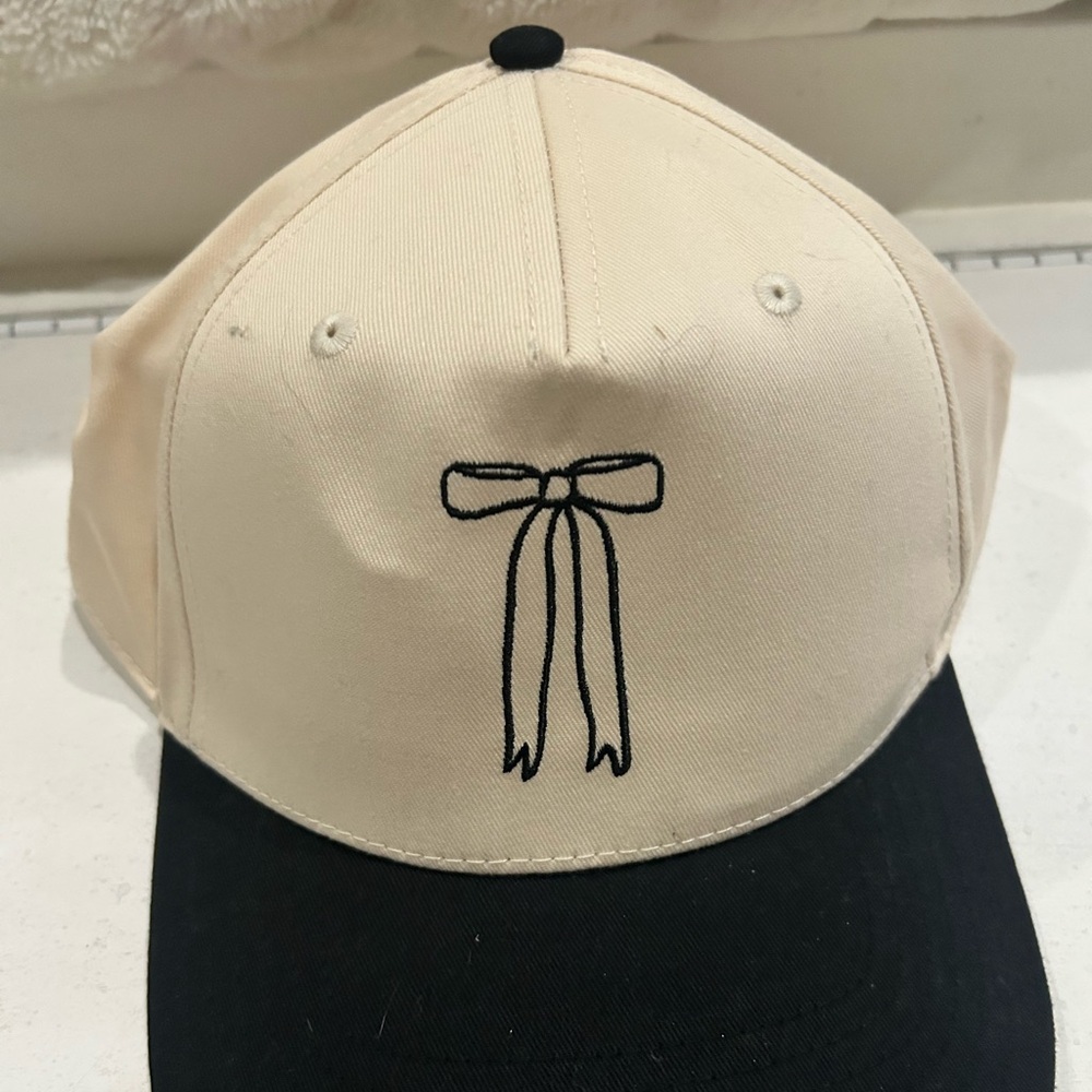 OTTO Cream Cap with Black Bow Accent.
Snap back. One size fits all.